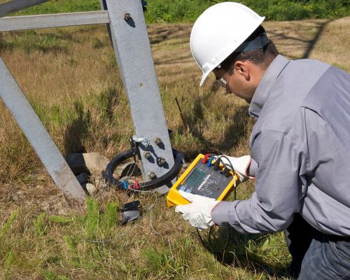 Electrician efectuând măsurători PRAM la un stâlp metalic de înaltă tensiune în aer liber