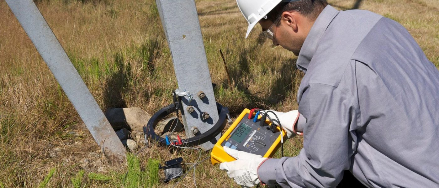 Electrician efectuând măsurători PRAM la un stâlp metalic de înaltă tensiune în aer liber